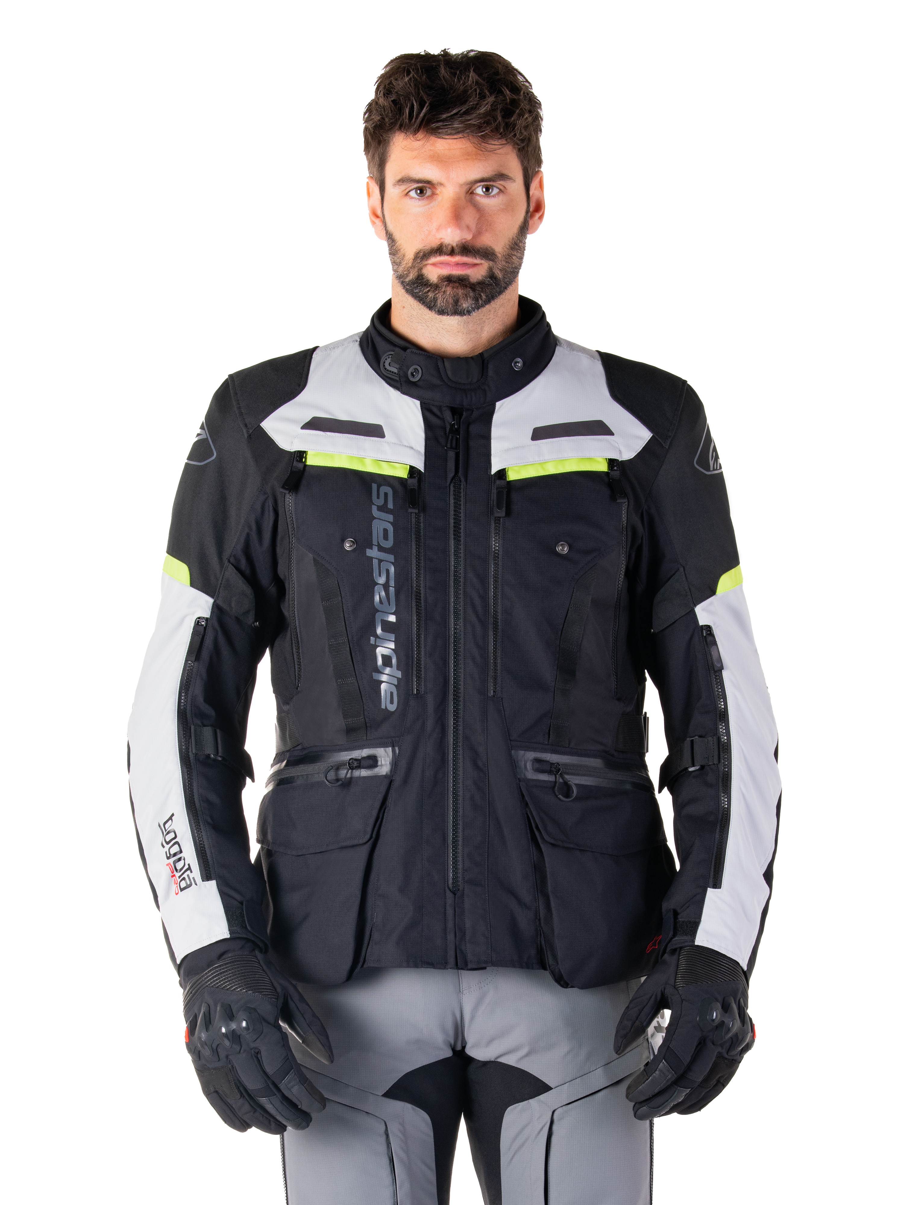 Man som bär Alpinestars Bogotá Pro Drystar®-jacka i färgerna svart, isgrå och neongul, allväders motorcykeljacka för adventure-touring, vattentät design med flera fickor och vertikal logotyp, matchad med svarta handskar och grå körbyxor