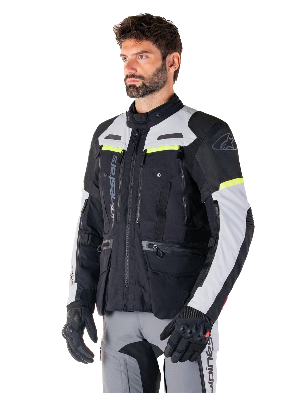 Alpinestars Bogotá Pro Drystar®-jacka, motorcykeljacka för adventure touring, Black Ice Gray och Yellow Fluo, bärs av en man med matchande grå byxor och svarta handskar, med tekniska ventilationspaneler och design med flera fickor.