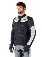 Alpinestars Bogotá Pro Drystar®-jacka, motorcykeljacka för adventure touring, Black Ice Gray och Yellow Fluo, bärs av en man med matchande grå byxor och svarta handskar, med tekniska ventilationspaneler och design med flera fickor.