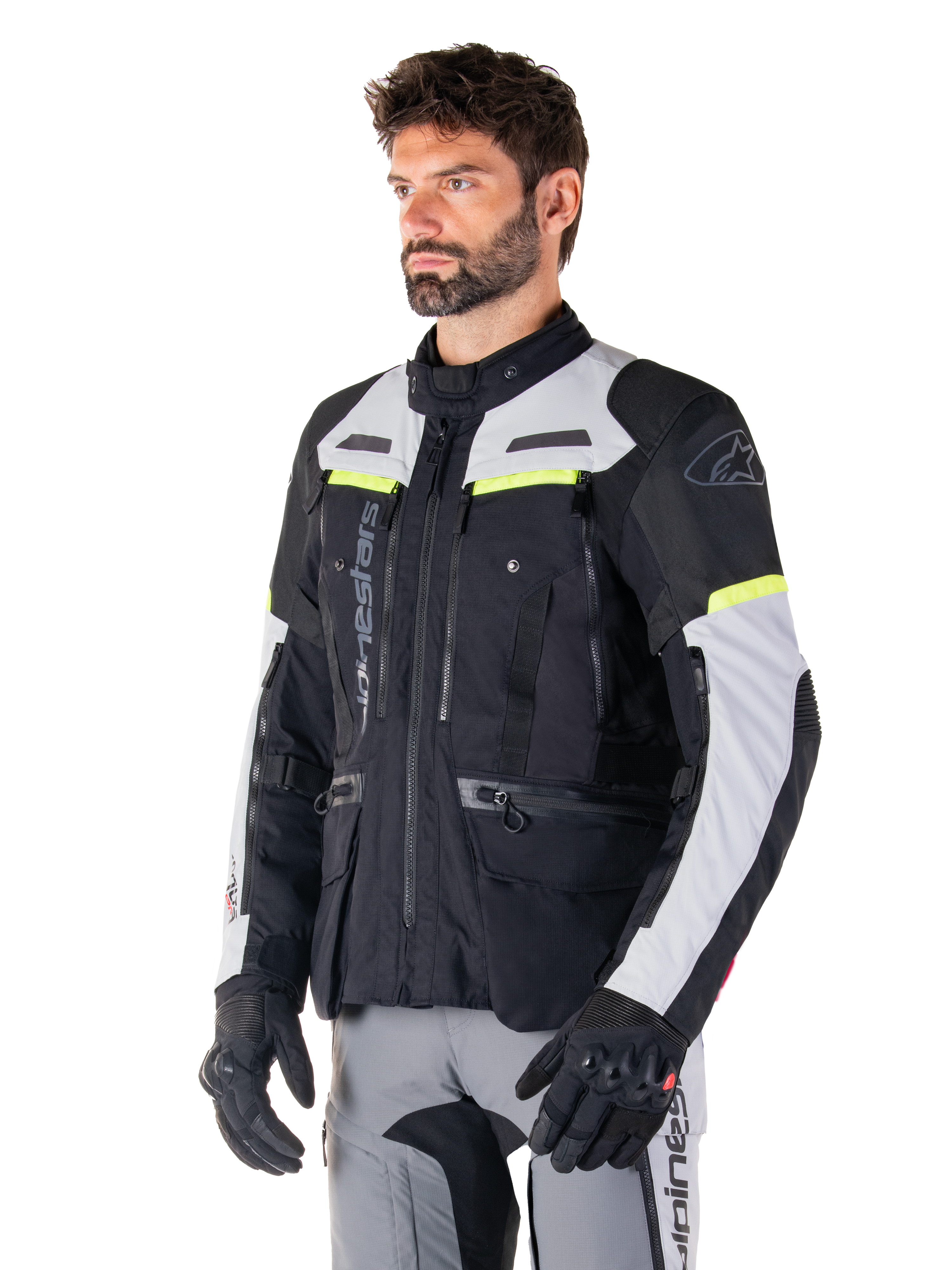 Alpinestars Bogotá Pro Drystar®-jacka, motorcykeljacka för adventure touring, Black Ice Gray och Yellow Fluo, bärs av en man med matchande grå byxor och svarta handskar, med tekniska ventilationspaneler och design med flera fickor.