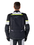 Alpinestars Bogota' Pro Drystar®-jacka, motorcykeljacka för adventure touring, svart, isgrå och fluorescerande gul, vy bakifrån som visar 'TECH TOURING'-märkning på en fluorescerande gul rand, stor ventilationspanel på ryggen och justerbara midjeremmar, teknisk allvädersutrustning