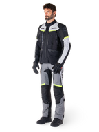 Alpinestars Bogotá Pro Drystar®-jacka, motorcykeljacka för adventure touring, Black Ice Gray Yellow Fluo, bärs av modell med matchande byxor och svarta handskar, med vattentät textilkonstruktion, ventilationspaneler och fluorescerande detaljer.