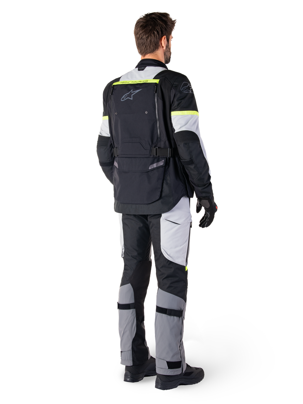 Bakifrån på en förare som bär Alpinestars Bogotá Pro Drystar®-jacka i Black Ice Gray Yellow Fluo, kombinerad med matchande adventure touring-byxor, med en stor ryggficka och gula fluorescerande detaljer, textilmotorcykelutrustning för alla säsonger.