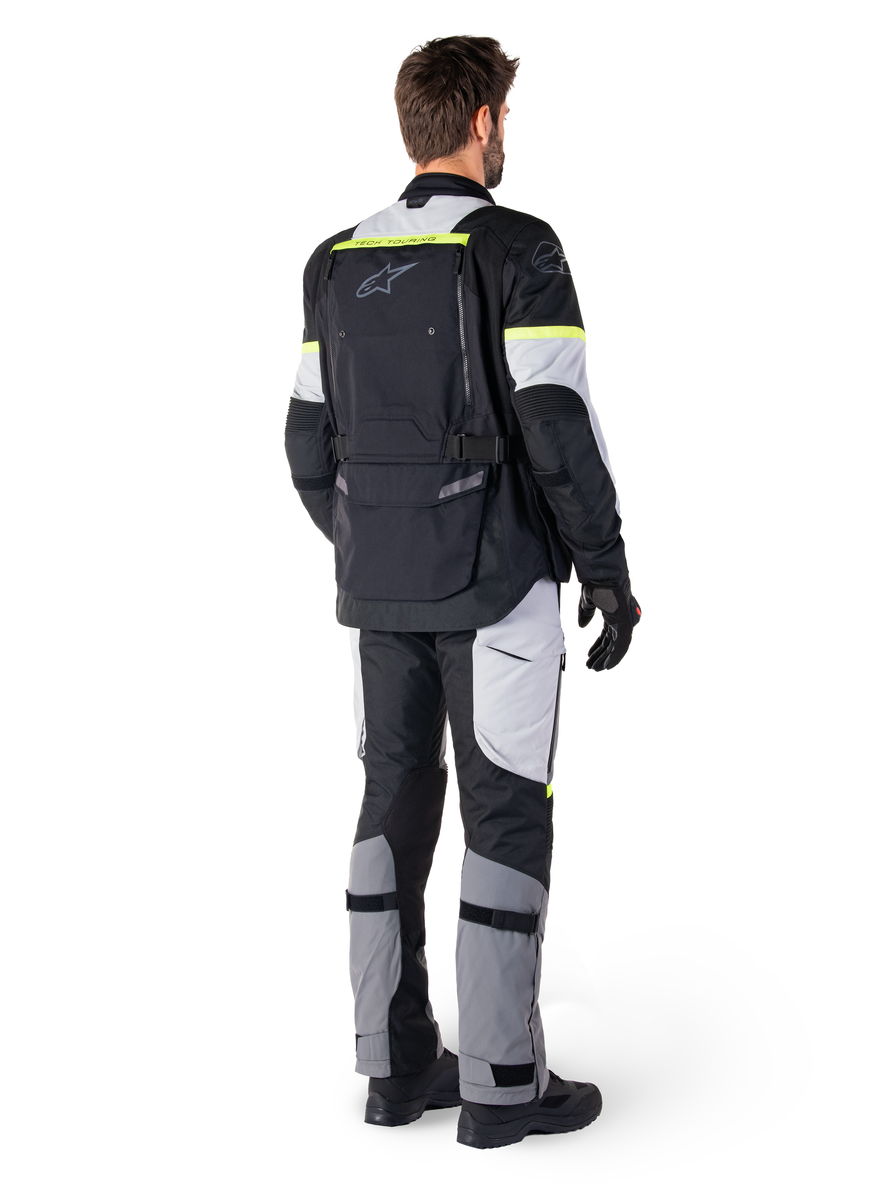 Bakifrån på en förare som bär Alpinestars Bogotá Pro Drystar®-jacka i Black Ice Gray Yellow Fluo, kombinerad med matchande adventure touring-byxor, med en stor ryggficka och gula fluorescerande detaljer, textilmotorcykelutrustning för alla säsonger.