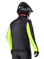 Alpinestars Bogotá Pro Drystar®-jacka, vy bakifrån, svart med gul fluo-ärmar, bärs av en förare med svart hjälm och handskar, hög synlighet motorcykelutrustning för äventyrstouring med teknisk textilfinish.