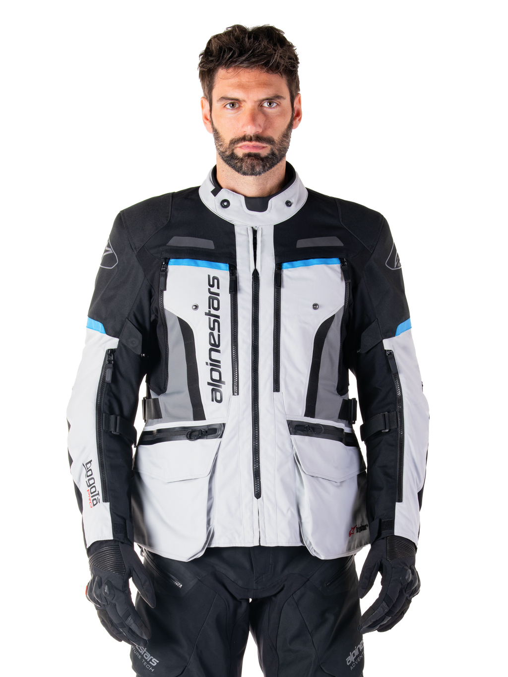 Alpinestars Bogota Pro Drystar-jacka, Adventure Touring-motorcykeljacka, isgrå med svarta och cyanblå detaljer, vy framifrån som visar ventilationspaneler och cargofickor, bärs av en modell med svarta mc-byxor och handskar