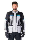 Alpinestars Bogota Pro Drystar-jacka, Adventure Touring-motorcykeljacka, isgrå med svarta och cyanblå detaljer, vy framifrån som visar ventilationspaneler och cargofickor, bärs av en modell med svarta mc-byxor och handskar