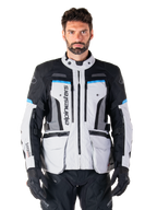Alpinestars Bogota Pro Drystar-jacka, Adventure Touring-motorcykeljacka, isgrå med svarta och cyanblå detaljer, vy framifrån som visar ventilationspaneler och cargofickor, bärs av en modell med svarta mc-byxor och handskar