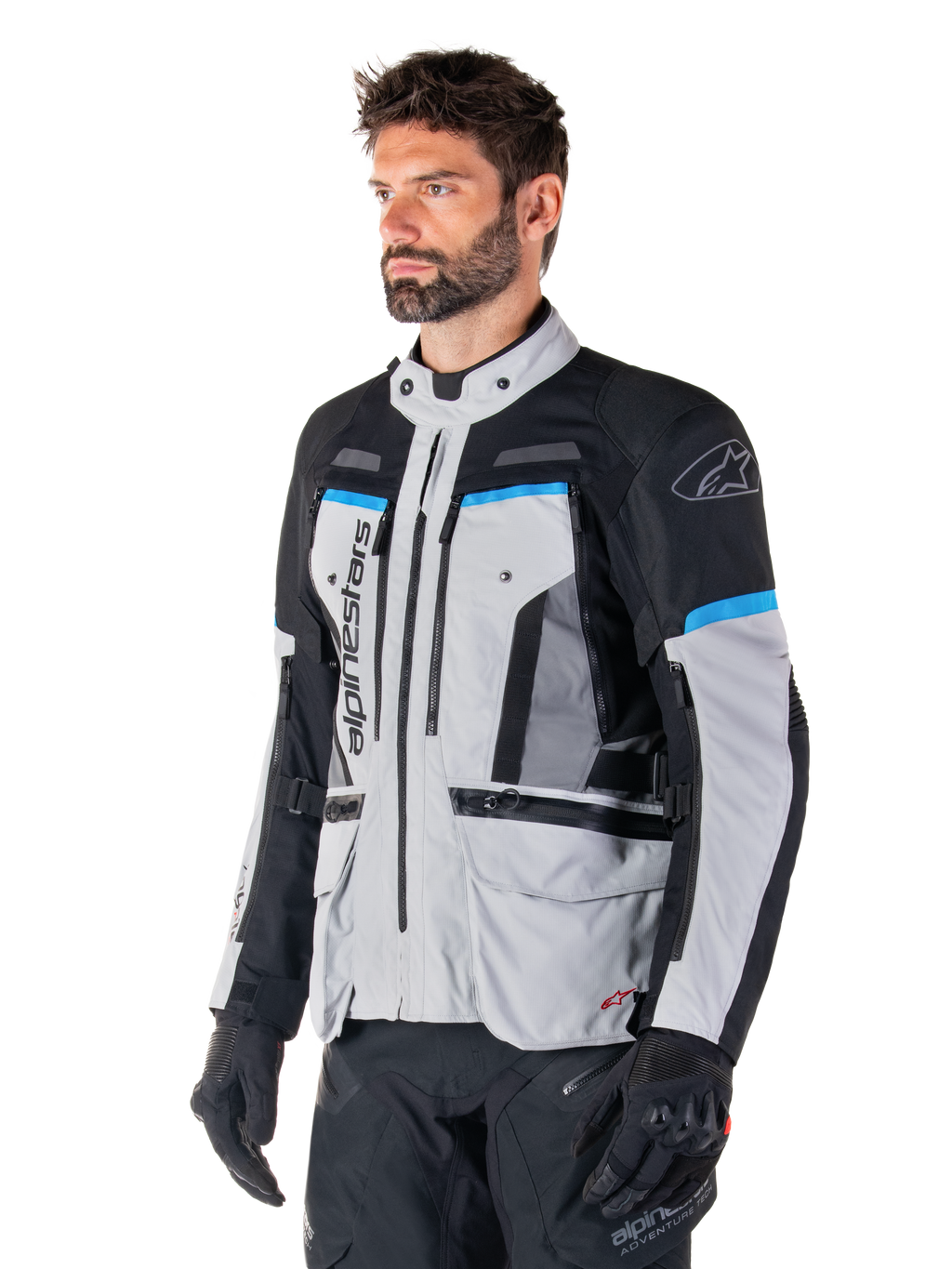 Alpinestars Bogota' Pro Drystar®-jacka, Ice Gray, svart och cyan, adventure-motorcykeljacka som bärs av en man med svarta handskar, teknisk design med flera fickor och ventilationspaneler, högpresterande körutrustning
