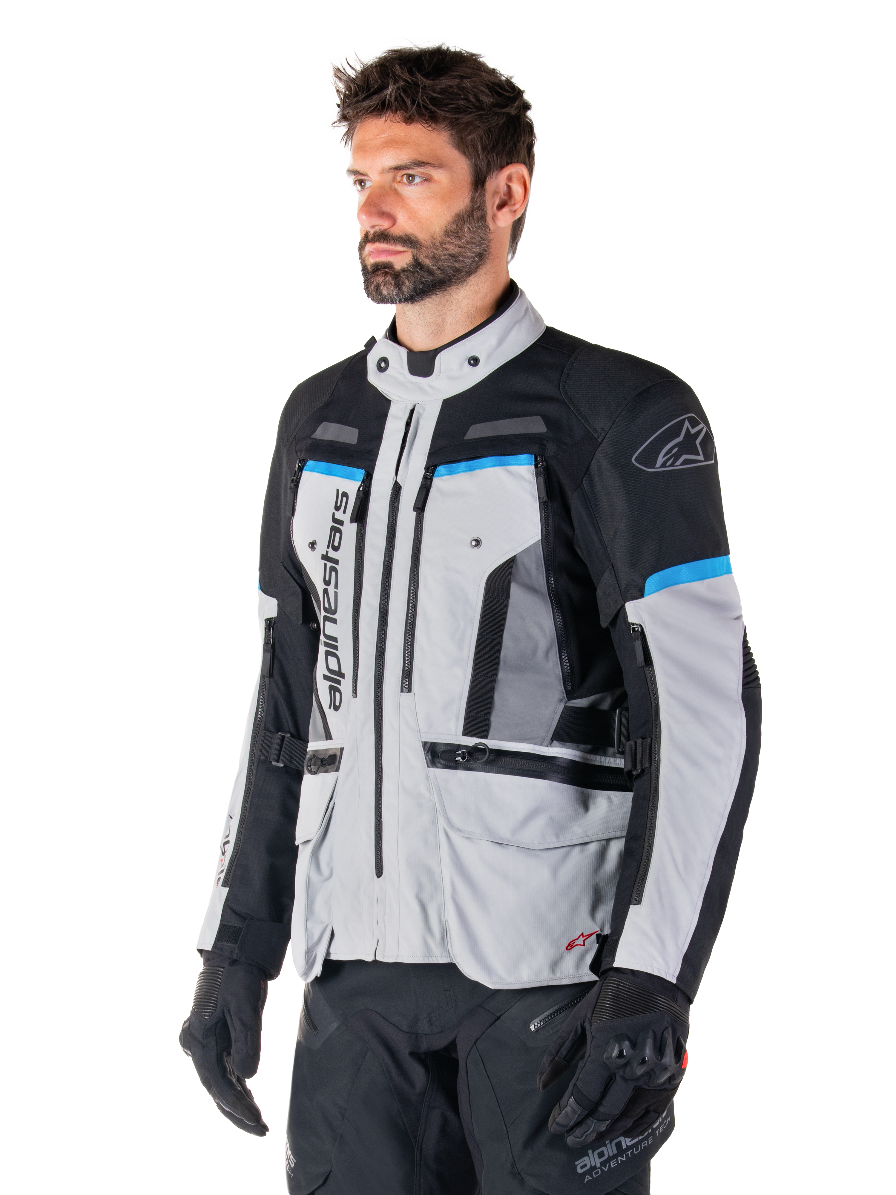 Alpinestars Bogota' Pro Drystar®-jacka, Ice Gray, svart och cyan, adventure-motorcykeljacka som bärs av en man med svarta handskar, teknisk design med flera fickor och ventilationspaneler, högpresterande körutrustning