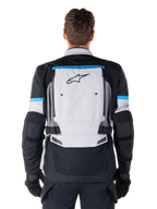 Alpinestars Bogota' Pro Drystar® jacka, äventyrsmotorcykeljacka, Ice Gray, svart och cyan, vy bakifrån med en stor ljusgrå panel med svart stjärnlogotyp, cyanfärgade detaljer med Tech Touring-branding och justerbara midjeremmar
