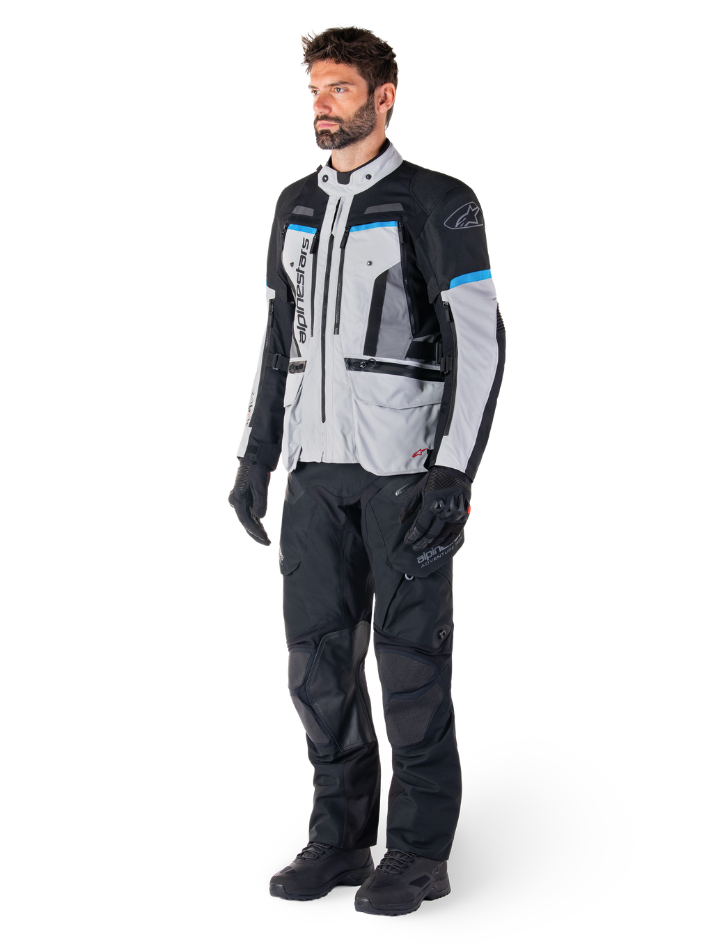 Manlig förare i Alpinestars Bogotá Pro Drystar®-jacka i Ice Gray, svart och cyan, matchad med svarta tekniska körbyxor och handskar, äventyrstouringutrustning för prestanda i alla väder