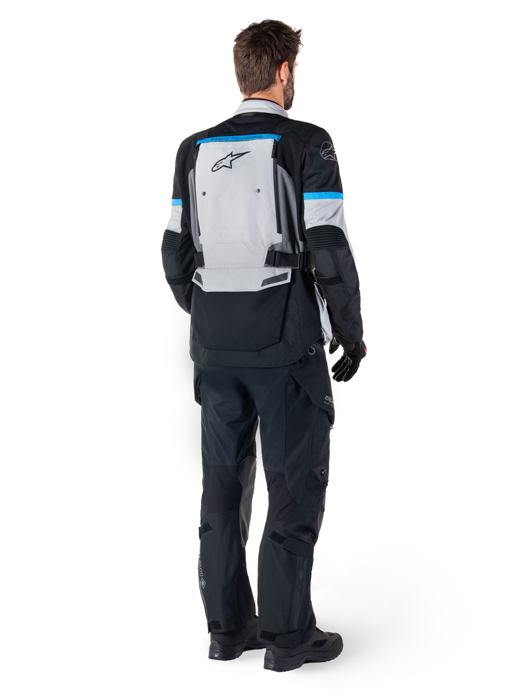 Alpinestars Bogota' Pro Drystar® jacka, äventyrsmotorcykeljacka, isgrå, svart och cyan, sedd bakifrån buren med matchande svarta byxor och handskar, med en stor grå ryggpanel med svart Alpinestars-logotyp och cyanblå accenter.