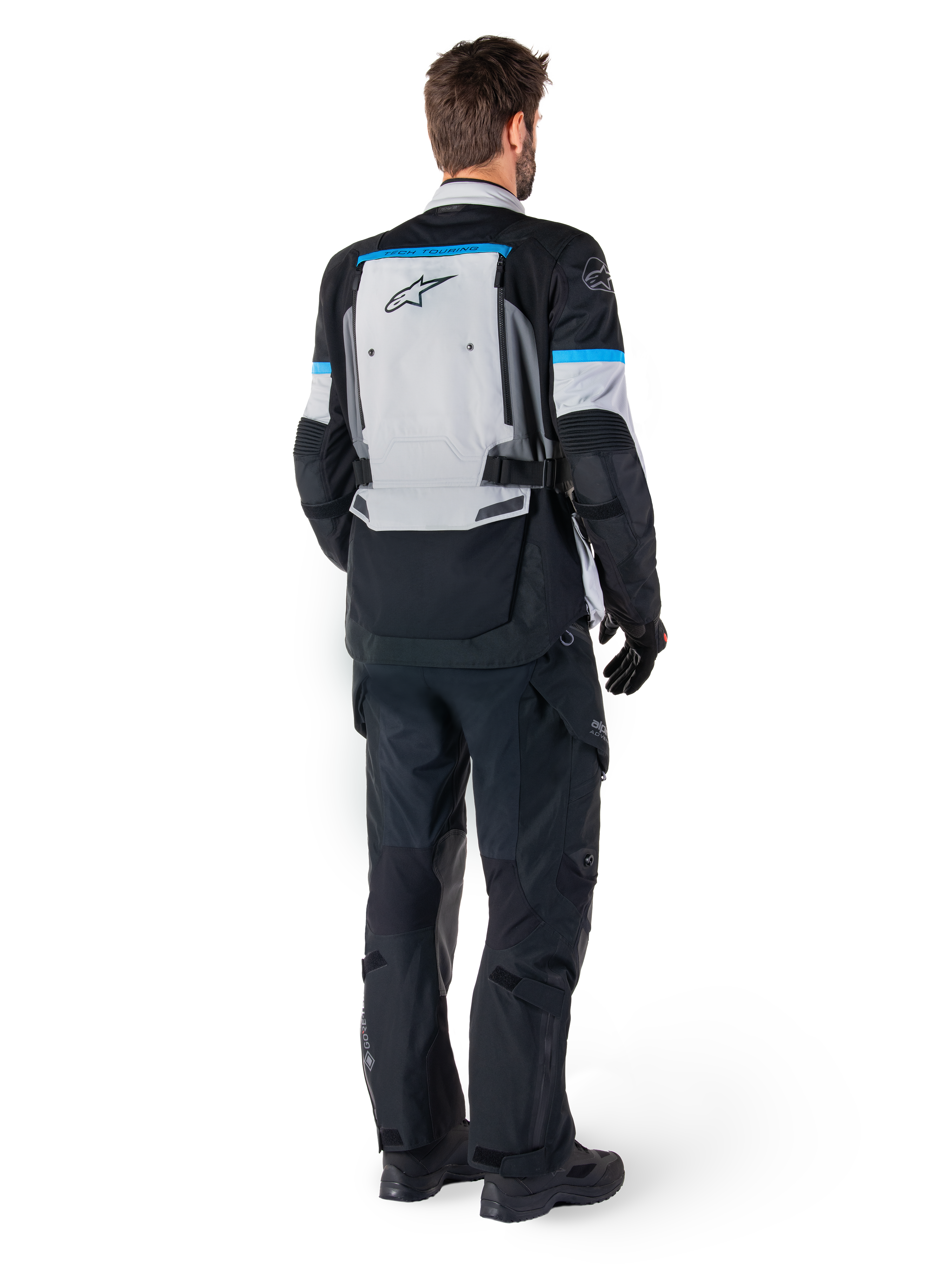 Alpinestars Bogota' Pro Drystar® jacka, äventyrsmotorcykeljacka, isgrå, svart och cyan, sedd bakifrån buren med matchande svarta byxor och handskar, med en stor grå ryggpanel med svart Alpinestars-logotyp och cyanblå accenter.