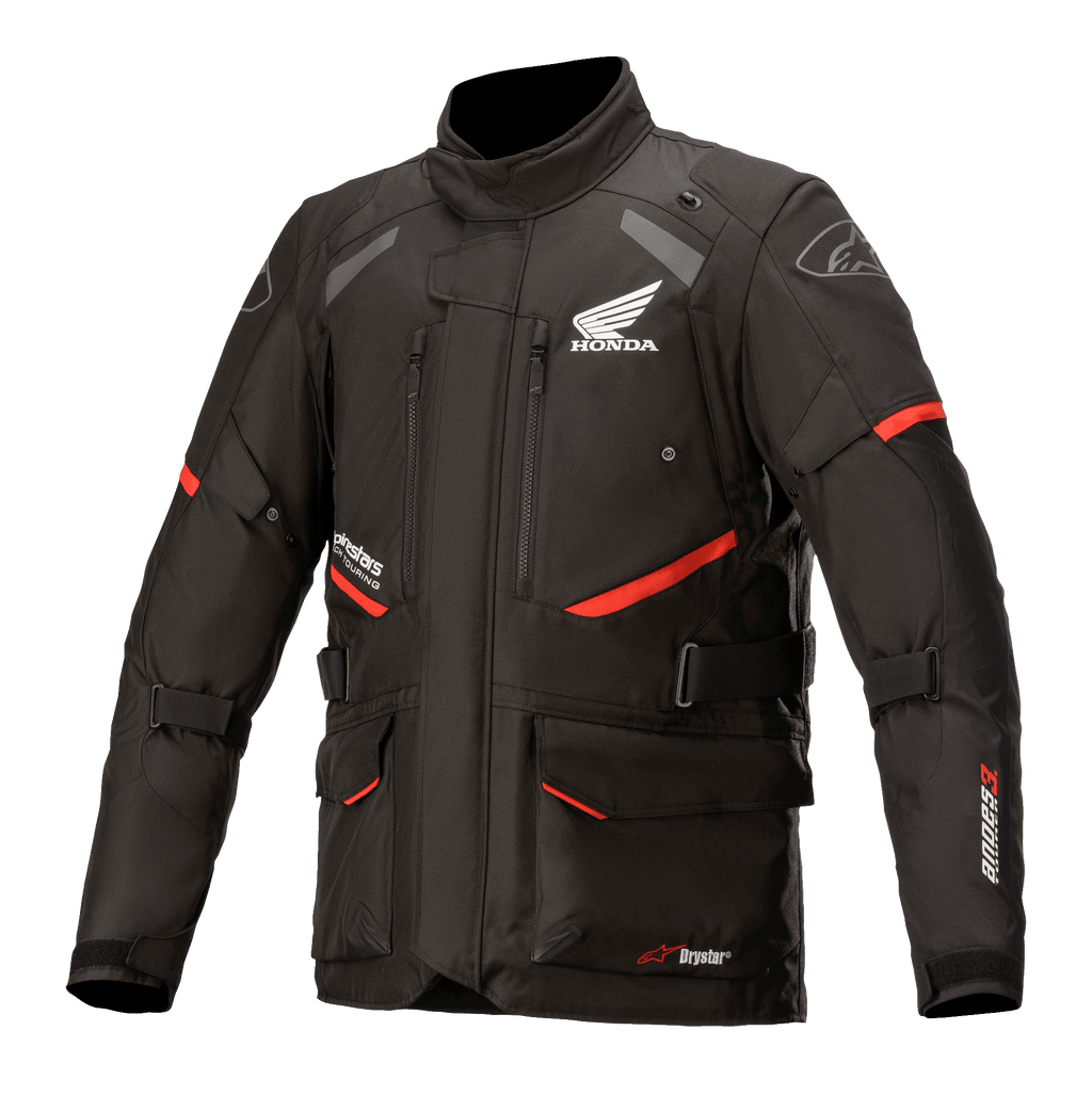 Honda Andes V3 Drystar-jacka, motorcykeljacka för touring, svart med röda accenter, vy framifrån med stora cargofickor och justerbara remmar, teknisk textilkonstruktion med Honda-vinge och Alpinestars-logotyper, äventyrsinspirerad design