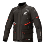 Honda Andes V3 Drystar-jacka, motorcykeljacka för touring, svart med röda accenter, vy framifrån med stora cargofickor och justerbara remmar, teknisk textilkonstruktion med Honda-vinge och Alpinestars-logotyper, äventyrsinspirerad design