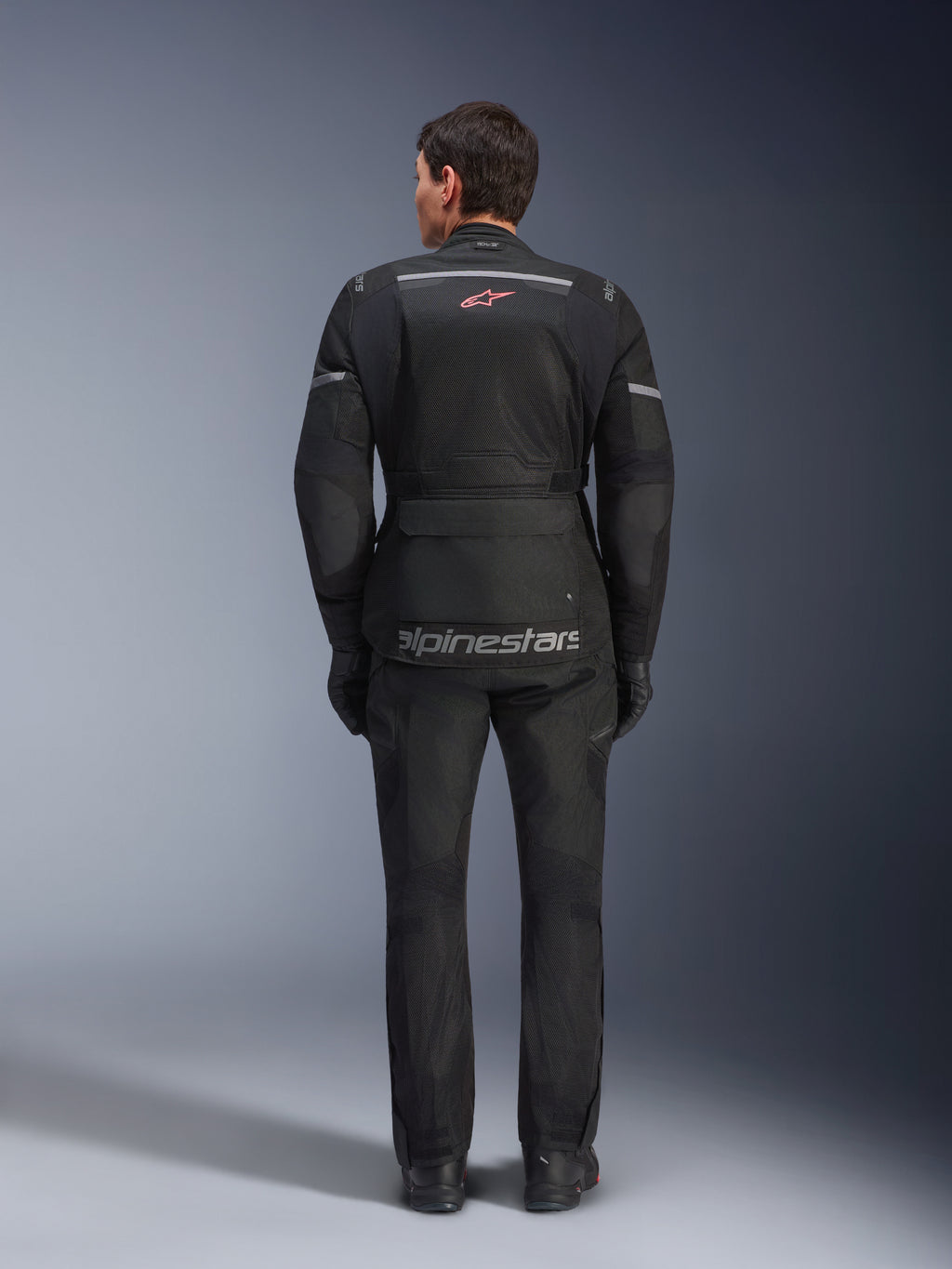 Rear view of a rider wearing the Alpinestars Andes Air Drystar® Jacket in Black, featuring extensive mesh ventilation panels on the back, red Alpinestars logo, and reflective accents, paired with matching motorcycle pants and gloves for adventure touring.