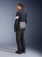 Manlig modell sedd snett bakifrån bärandes Alpinestars Andes Air Drystar®-jacka i Deep Blue Black Ice Gray, matchad med svarta motorcykelbyxor och handskar, med en blå ryggpanel i mesh, grå praktisk ficka på nedre delen av ryggen och röda detaljer på ärmarna, professionell touringutrustning för äventyrskörning.