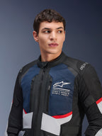 Alpinestars Andes Air Drystar®-jacka, motorcykeljacka, mörkblå, svart och isgrå med röda accenter, bärs av manlig modell, med ventilerade meshpaneler på bröstet, vit stjärnlogotyp med utforskningskoordinater och väganpassad äventyrsdesign