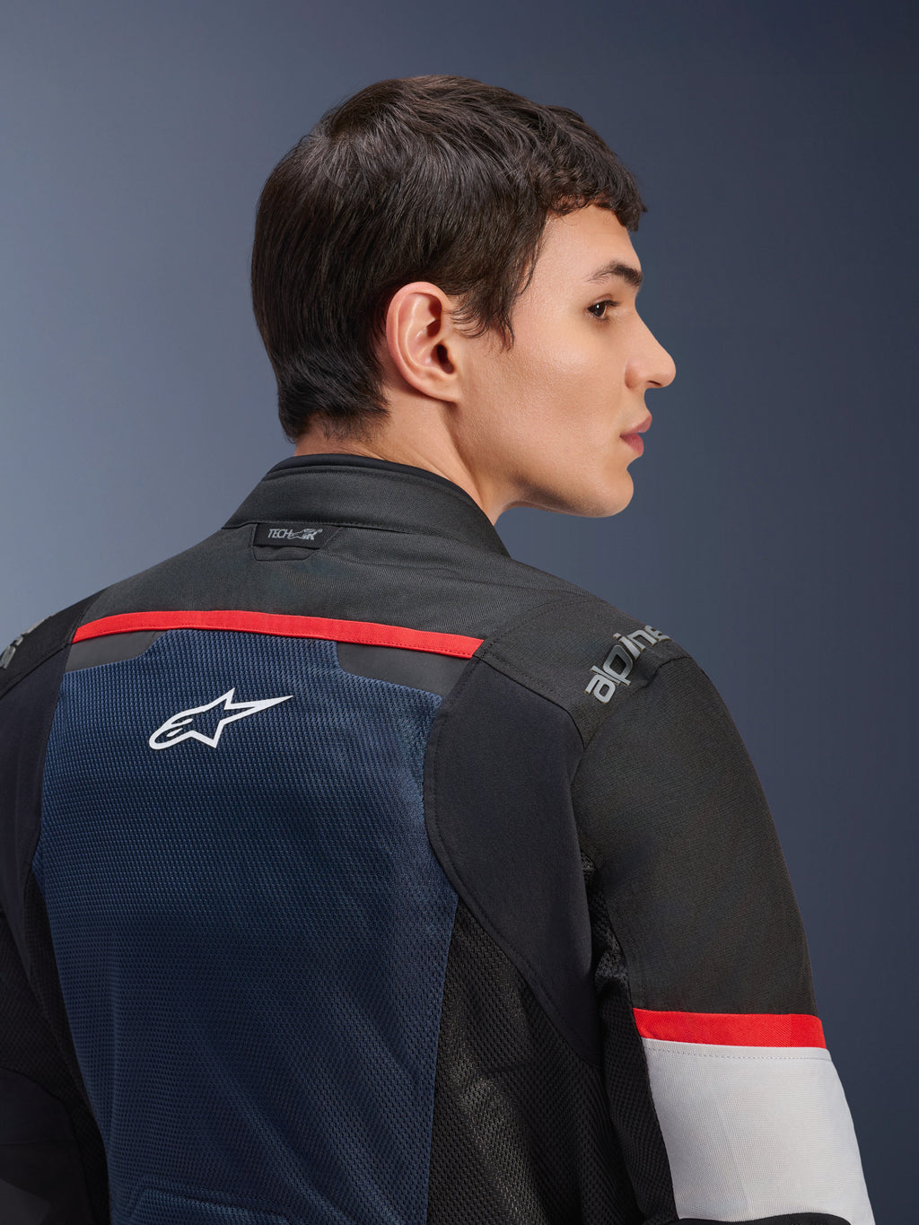 Alpinestars Andes Air Drystar®-jacka, Deep Blue Black och Ice Gray, närbild bakifrån på en modell, med en ventilerande meshpanel med vit stjärnlogotyp, röda detaljer och Tech-Air®-märkning på kragen, touring-motorcykelutrustning för två säsonger