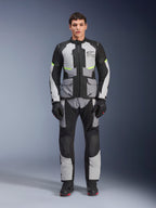 Alpinestars Andes Air Drystar® jacka i Ice Gray, mörkgrått och svart, buren av en manlig modell med matchande mc-byxor och handskar, adventure touring-design med stora framfickor och fluorescerande gula detaljer, studiobild framifrån