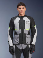 Manlig förare som bär Alpinestars Andes Air Drystar®-jacka i Ice Gray, Dark Gray och svart, med neongula detaljer och ventilationspaneler i mesh, stylad med matchande motorcykelbyxor och handskar, adventure touring-utrustning