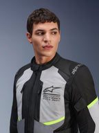 Alpinestars Andes Air Drystar®-jacka, MC-touringjacka, isgrå och mörkgrå med neongula detaljer, bärs av en manlig modell, med 2D-meshpaneler för ventilation, Alpinestars-logotyp med koordinater på bröstet och hållbar textilkonstruktion.