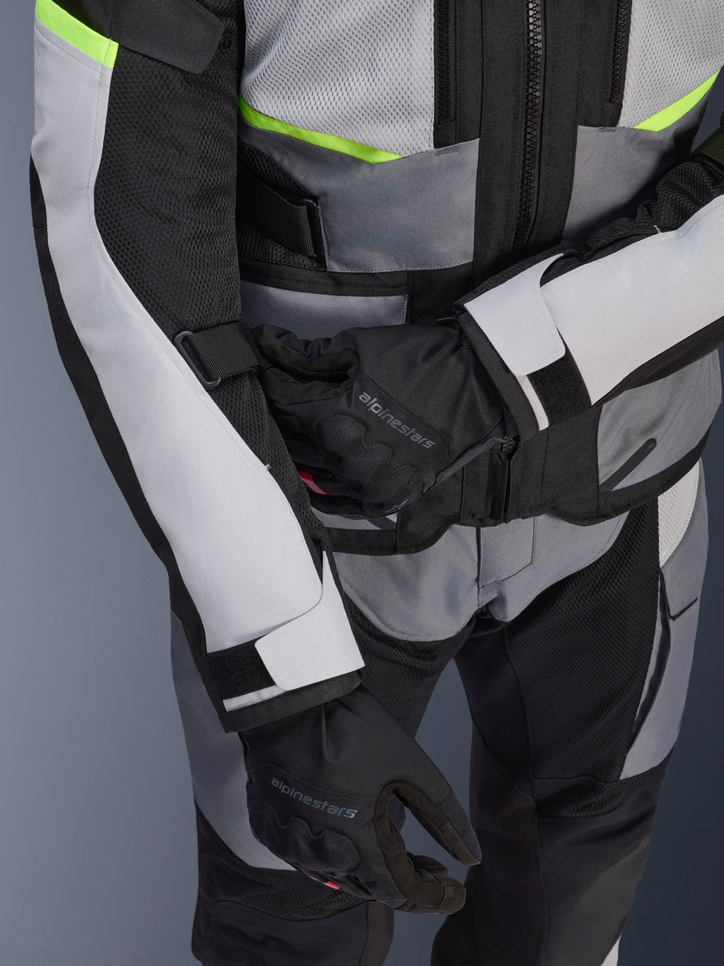 Alpinestars Andes Air Drystar® jacka, touringjacka för motorcykel, isgrå och mörkgrå med neongula detaljer, närbild som visar meshpaneler och justeringsremmar, bärs tillsammans med svarta Alpinestars-handskar