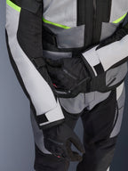 Alpinestars Andes Air Drystar® jacka, touringjacka för motorcykel, isgrå och mörkgrå med neongula detaljer, närbild som visar meshpaneler och justeringsremmar, bärs tillsammans med svarta Alpinestars-handskar