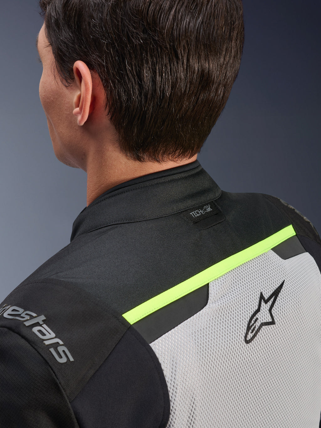 Alpinestars Andes Air Drystar®-jacka, motorcykeljacka i textil, Ice Gray, Dark Gray och svart, detaljvy bakifrån på övre ryggen och axeln, med ventilerande meshpaneler, fluorescerande gula accenter och Tech-Air-logotyp på kragen.