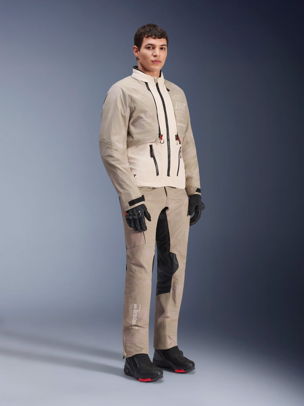 Alpinestars AMT-10LAB Drystar® XF-byxor och matchande jacka, Aluminum Camo-äventyrsutrustning, komplett outfit med svarta handskar och stövlar, med tekniska logotyper och modulära skyddspaneler, livsstilsbild i studiomiljö