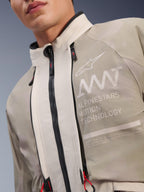 Alpinestars AMT-10LAB Drystar® XF-jacka, White Sand Aluminum Camo, närbild på bröstet med AMT Alpinestars Motion Technology-märkning, vattentäta dragkedjor med röda dragflikar och texturerat äventyrsredo textilmaterial.