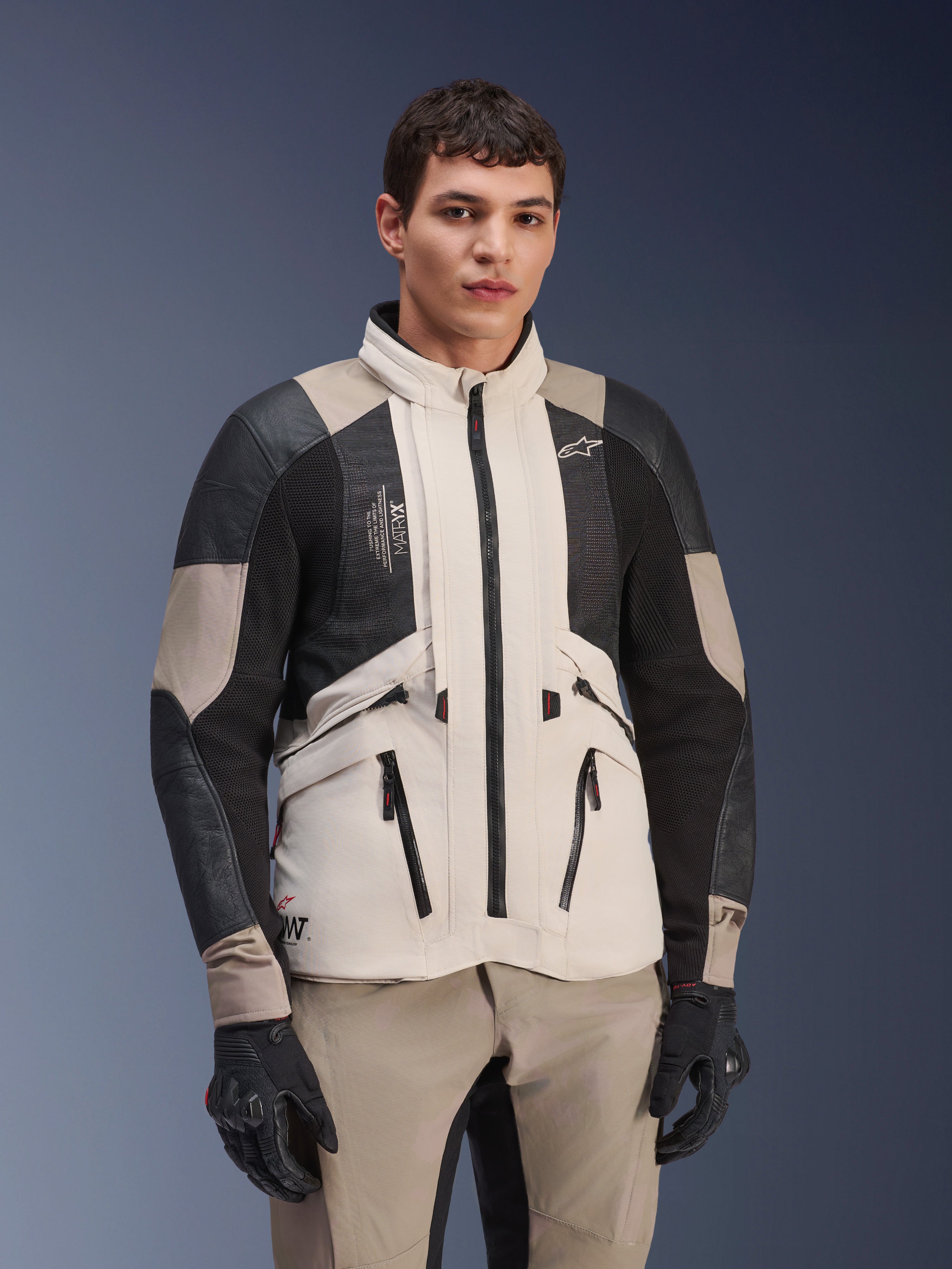 Alpinestars AMT-10LAB Drystar® XF-jacka, White Sand Aluminum Camo, äventyrsjacka för motorcykel med svarta MATRYX®-meshpaneler och läderförstärkningar, bärs av en modell med svarta handskar och matchande sandfärgade byxor, studioporträtt