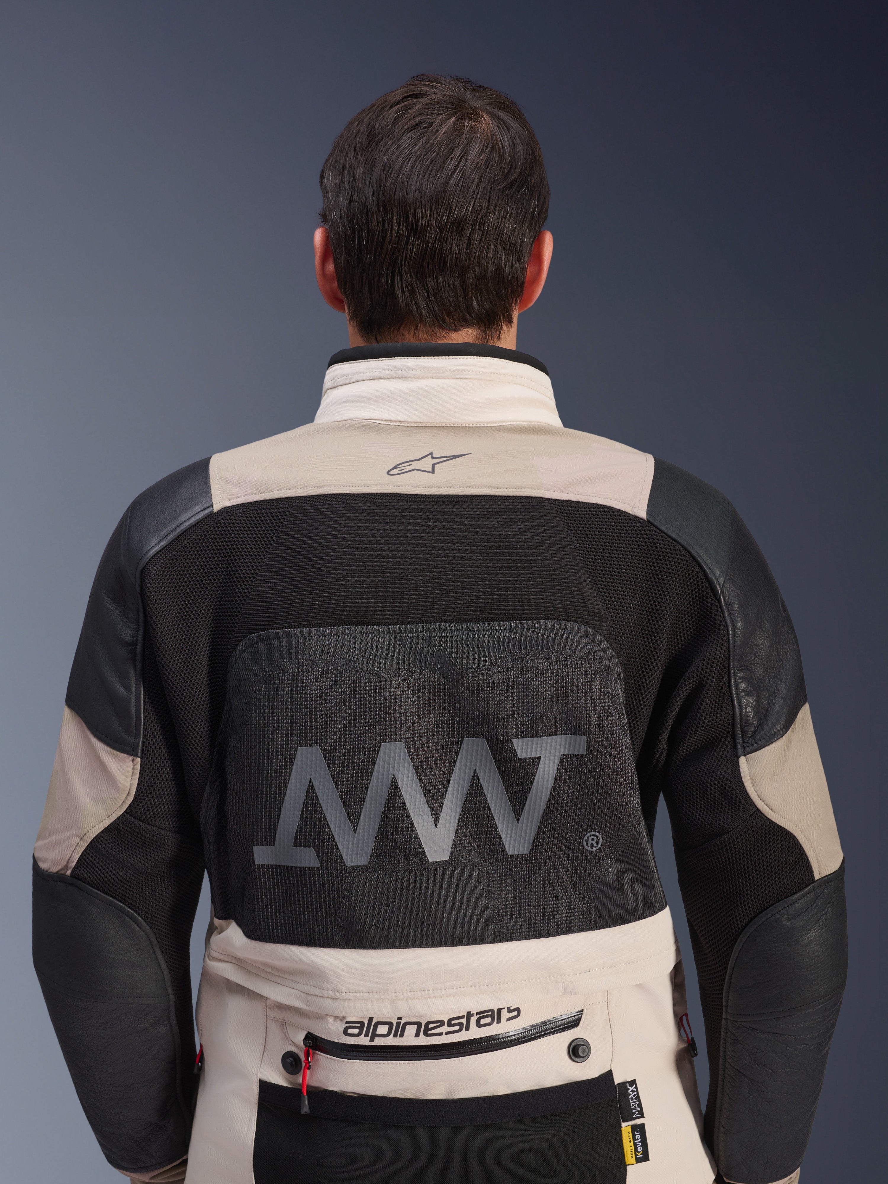 Vy bakifrån av Alpinestars AMT-10LAB Drystar® XF-jacka i färgerna White Sand och svart, med en stor AMT-logotyp på ryggpanelen i mesh, Alpinestars-branding på nedre delen av ryggen och teknisk textilkonstruktion för äventyrsmotorcykling