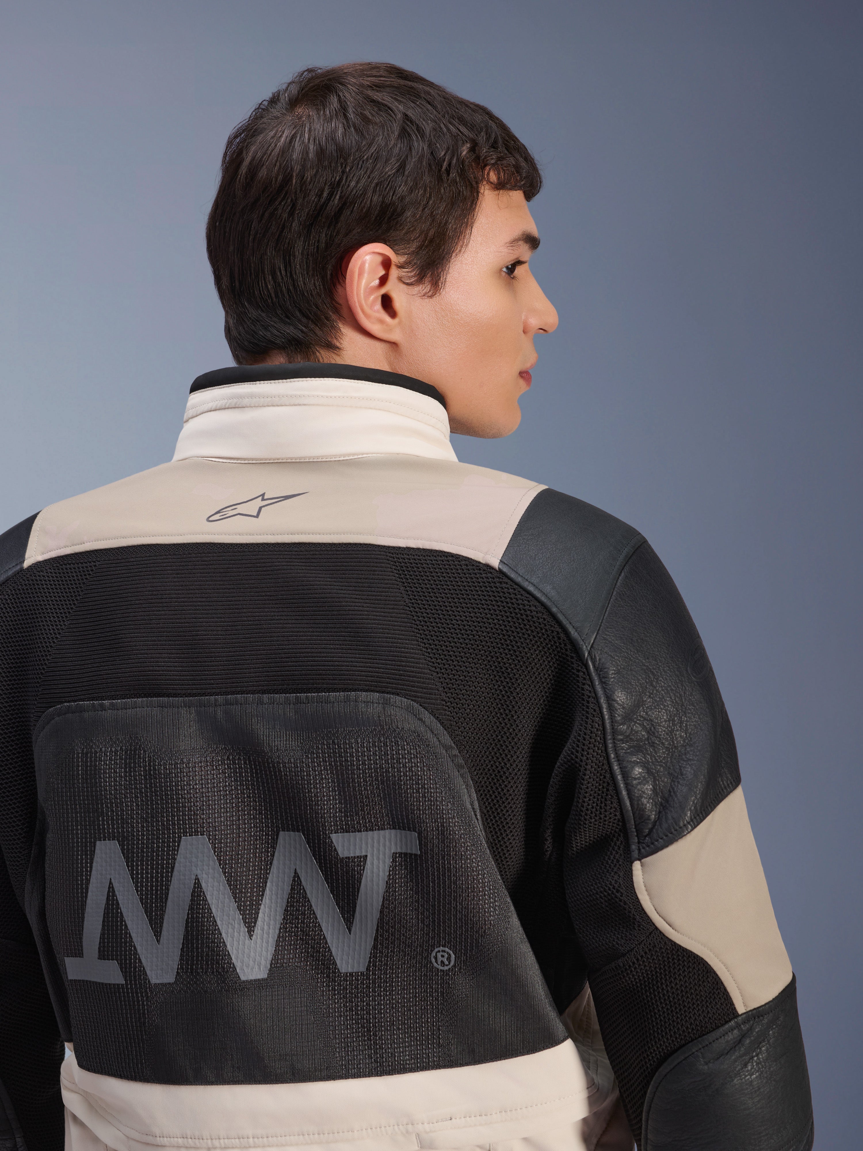 Alpinestars AMT-10LAB Drystar® XF-jacka, sedd bakifrån på manlig modell, färgkombinationen White Sand Aluminum Camo och svart, med stor AMT-logotyp, ventilationspaneler i mesh och läderförstärkningar, tekniska motorcykelkläder för äventyrskörning