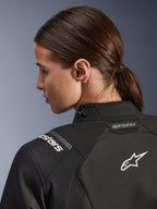 Alpinestars Stella Andes V4 Drystar®-jacka för dam, svart, närbild av övre ryggen och axeln, med vit broderad Astar-logotyp och märkning, teknisk textilkonstruktion för äventyrskörning med motorcykel