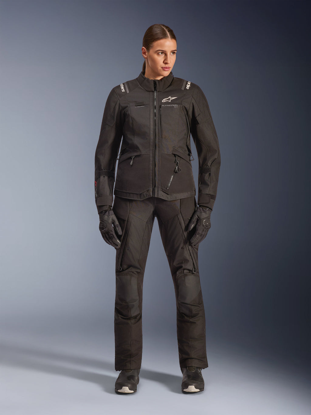 Kvinnlig förare i Alpinestars Stella Andes V4 Drystar®-jacka i svart, kombinerad med matchande svarta adventure-touringbyxor och handskar, teknisk textilkonstruktion med flera praktiska fickor och vit Alpinestars-logotyp, komplett motorcykelutrustning för alla väder