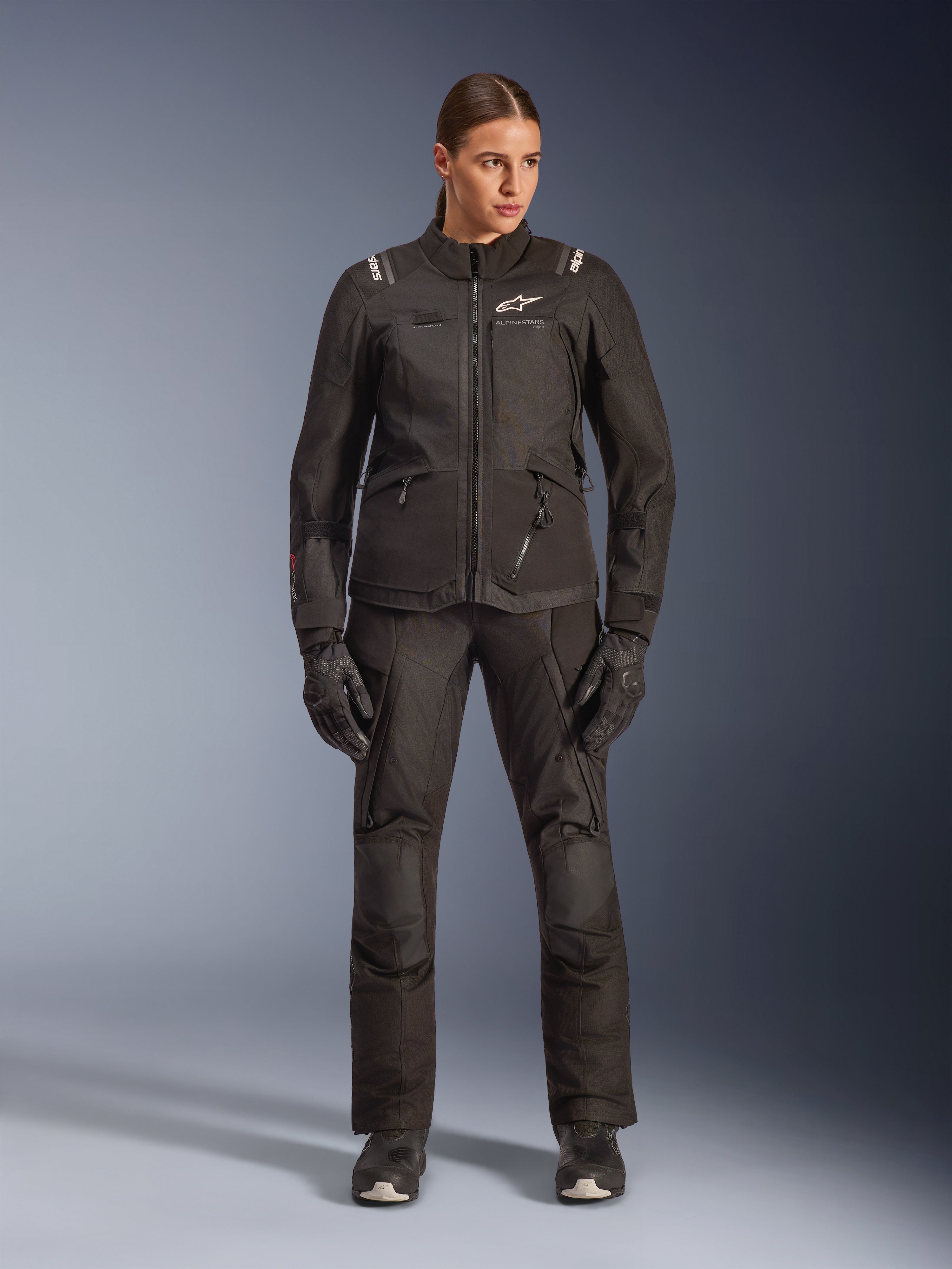 Kvinnlig förare i Alpinestars Stella Andes V4 Drystar®-jacka i svart, kombinerad med matchande svarta adventure-touringbyxor och handskar, teknisk textilkonstruktion med flera praktiska fickor och vit Alpinestars-logotyp, komplett motorcykelutrustning för alla väder