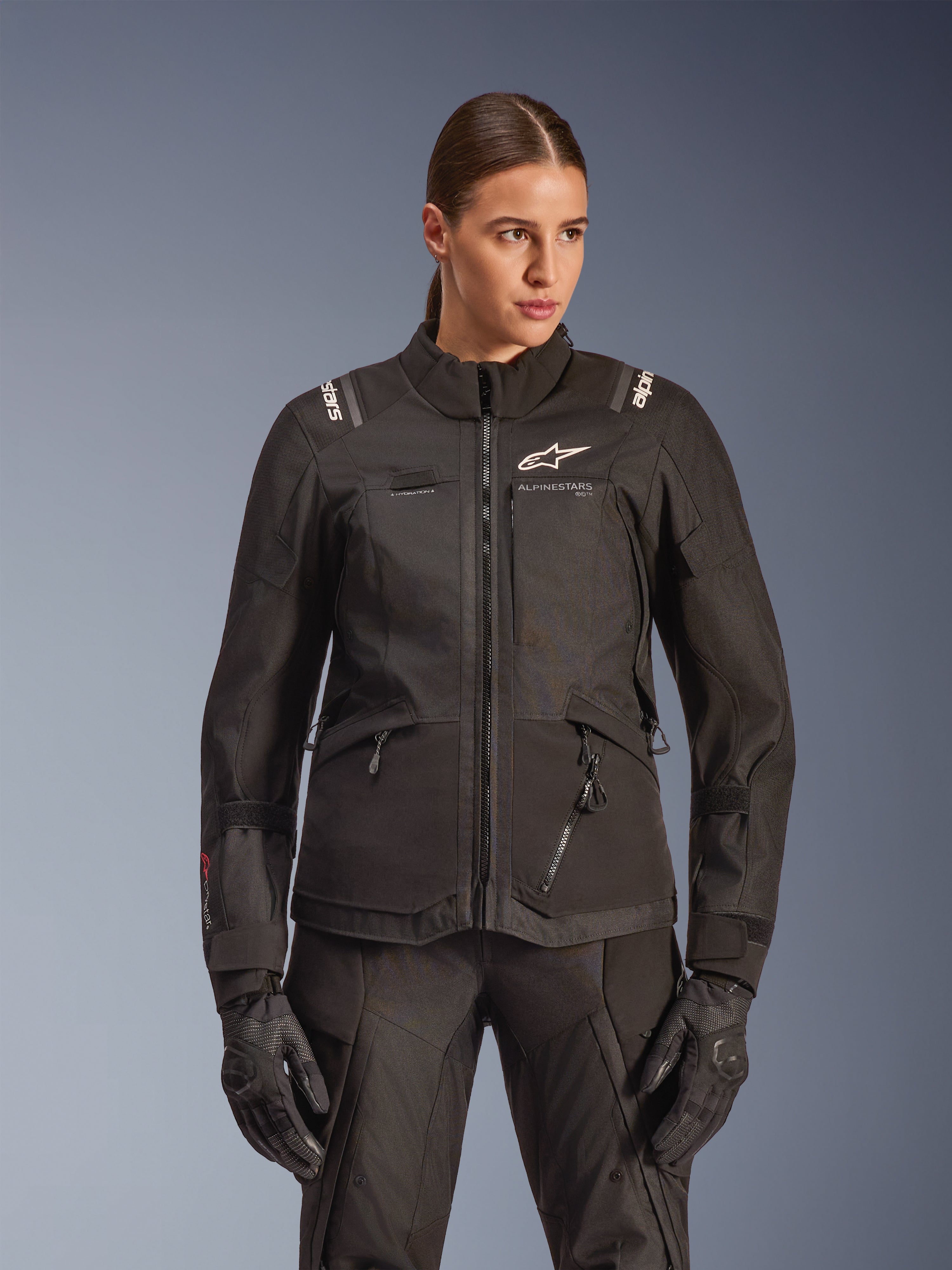 Alpinestars Stella Andes V4 Drystar jacka, motorcykeljacka för dam, svart, bärs av en modell med matchande körbyxor och handskar, med dragkedja fram, vit logotyp på bröstet och Alpinestars-branding på axlarna, smidig allvädersutrustning.