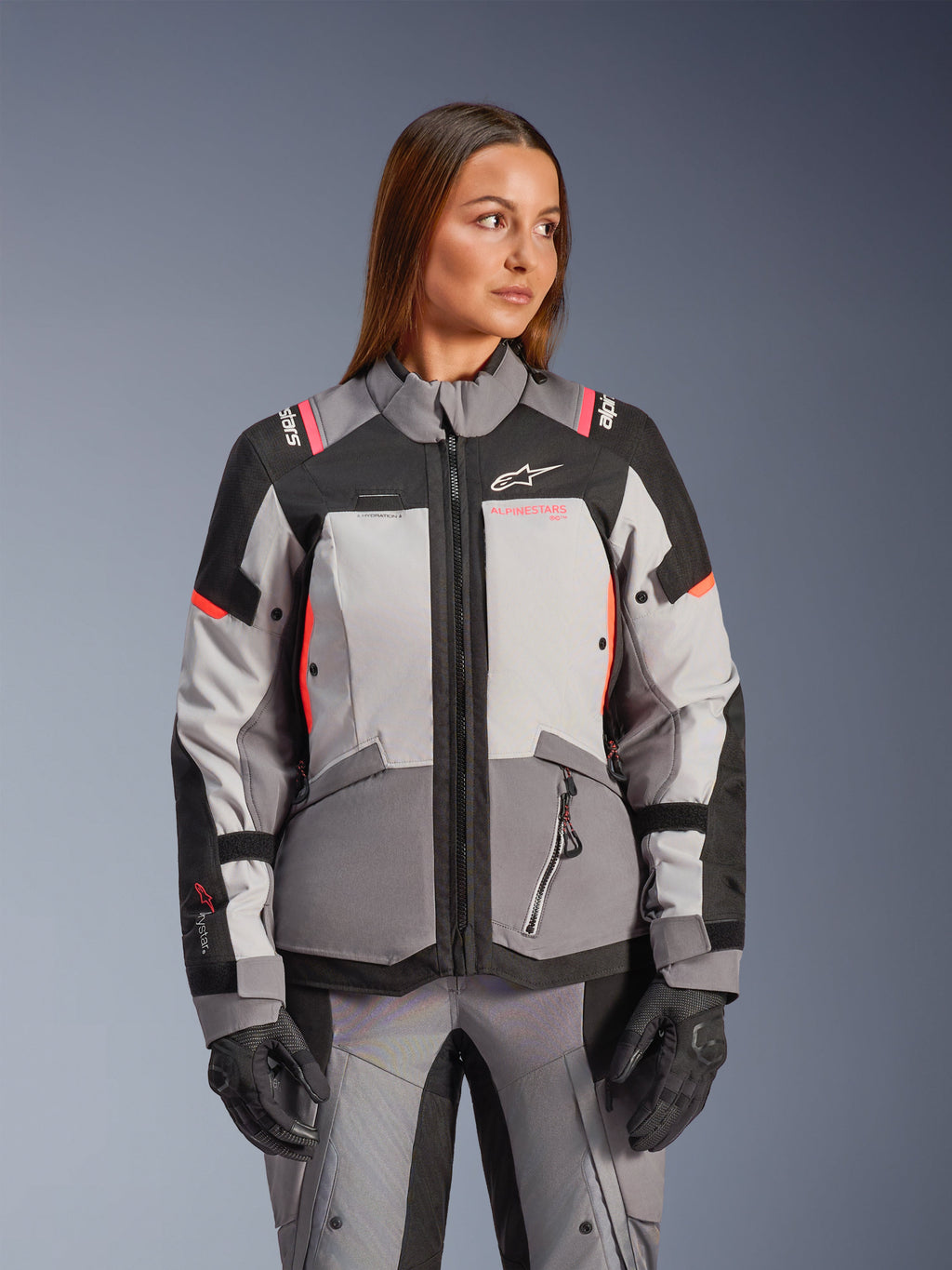 Alpinestars Stella Andes V4 Drystar® jacka, äventyrsinspirerad MC-jacka för dam, grå och svart med korallfärgade detaljer, vattentät textilkonstruktion, bärs av modell.