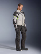 Alpinestars Stella Andes V4 Drystar®-jacka för dam, isgrå, mörkgrå och svart med fluorgula accenter, bärs av en kvinnlig modell med svarta motorcykelbyxor och handskar, skyddsutrustning för äventyrstouring för kvinnor