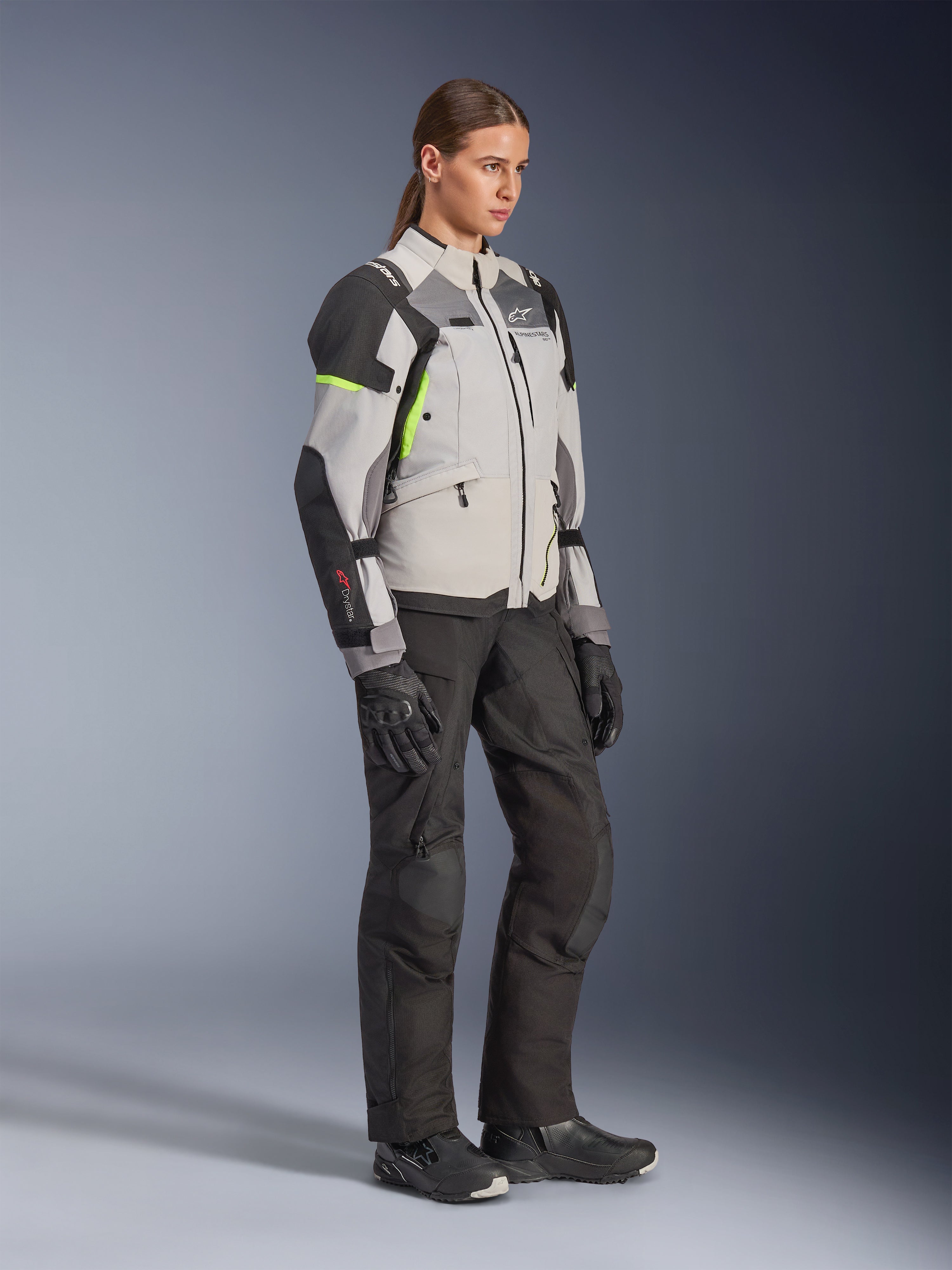 Alpinestars Stella Andes V4 Drystar®-jacka för dam, isgrå, mörkgrå och svart med fluorgula accenter, bärs av en kvinnlig modell med svarta motorcykelbyxor och handskar, skyddsutrustning för äventyrstouring för kvinnor