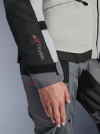 Alpinestars Stella Andes V4 Drystar®-jacka för dam, isgrå och mörkgrå, närbild med Drystar®-logotypen på den svarta ärmpanelen, justerbar kardborrestängning vid handleden och slitstark textilkonstruktion för adventure touring