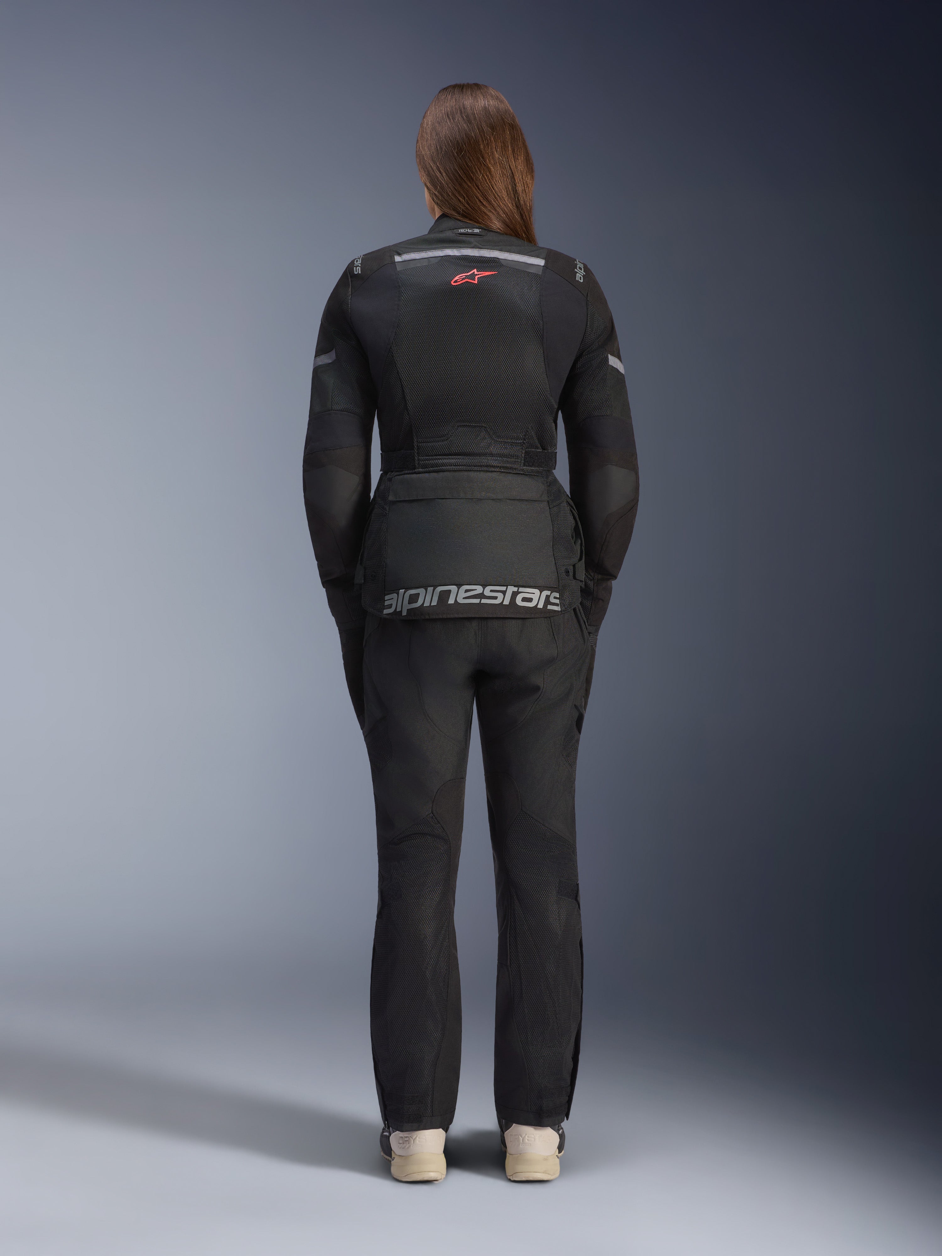 Kvinna i Alpinestars Stella Andes Air Drystar®-jacka och matchande byxor, svart, vy bakifrån som visar stor grå Alpinestars-logotyp på den nedre ryggfickan, liten röd stjärnlogotyp på övre ryggen, ventilationspaneler i mesh och reflexdetaljer för adventure touring