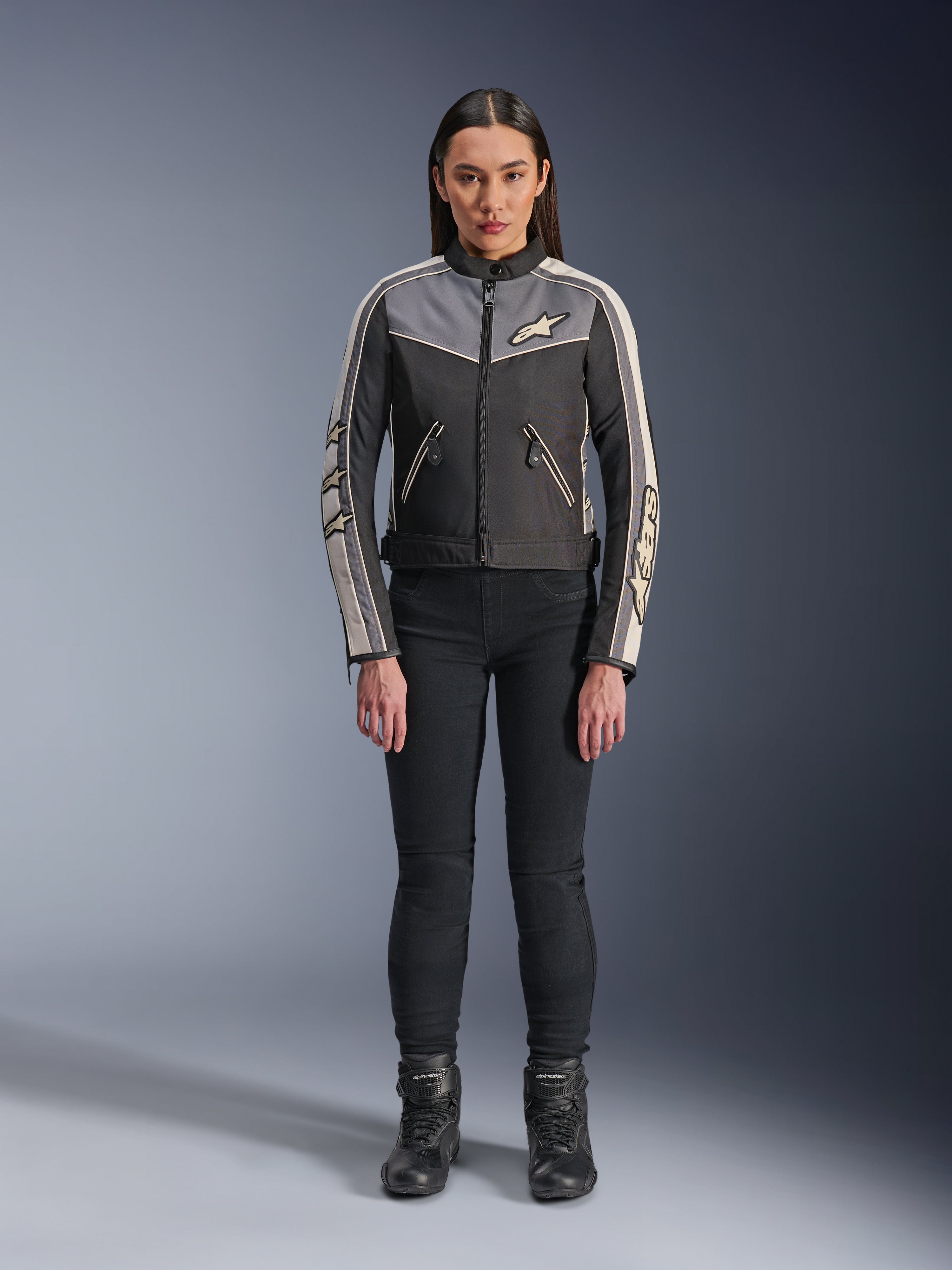 Woman wearing Alpinestars Stella T-Dyno WR Jacket, Black Dark Gray and Ecru, front view, textile motorcycle jacket with vintage-inspired design, featuring chest and sleeve branding, worn with black pants and boots