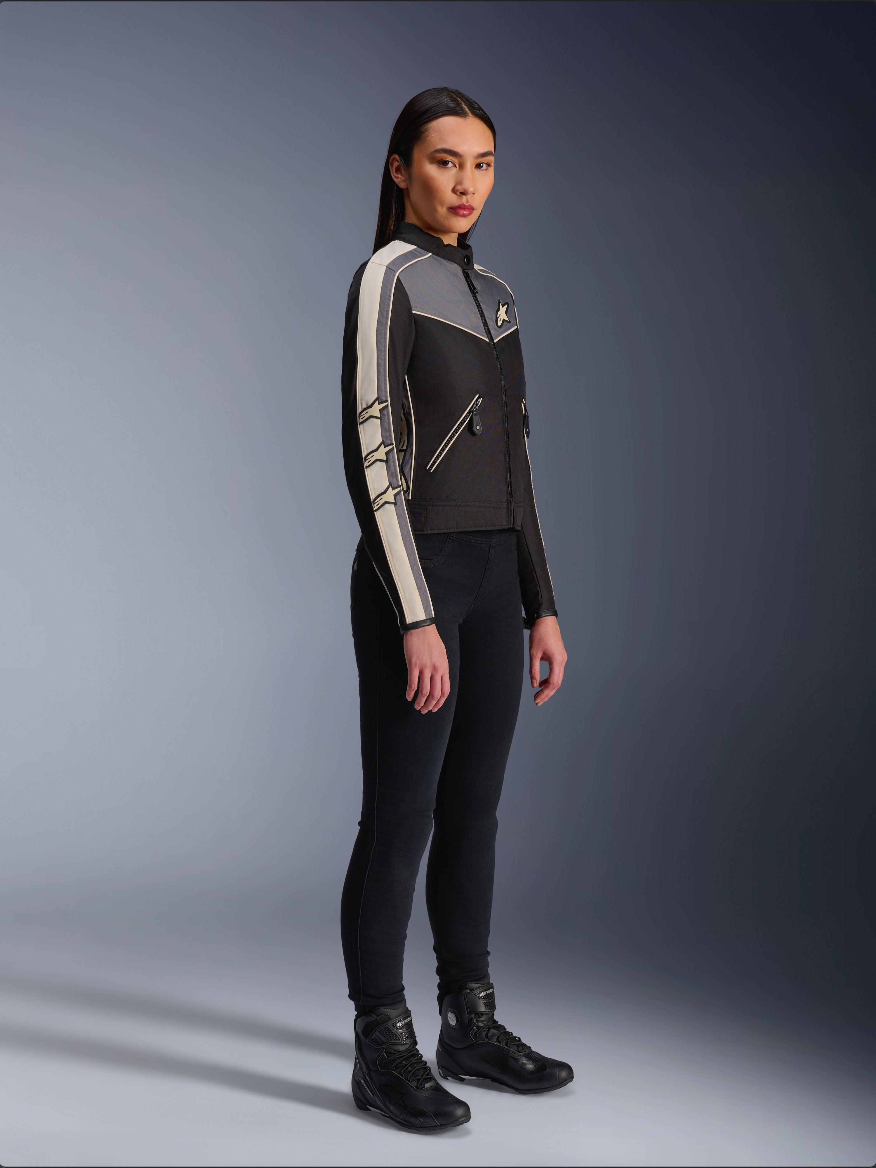 Alpinestars Stella T-Dyno WR Jacket, Women's textile motorcycle jacket, Black, Dark Gray, and Ecru, featuring vintage-inspired design with cream sleeve stripes and star logos, worn with black pants and riding boots, heritage-inspired urban riding gear