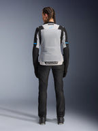 Alpinestars Stella ST-2 Air Jacket, Ice Gray Black, rear view on female model, featuring a large light gray mesh back panel, black sleeves with blue stripe accents, Alpinestars branding on the lower back, paired with black technical riding pants and boots, summer motorcycle touring gear