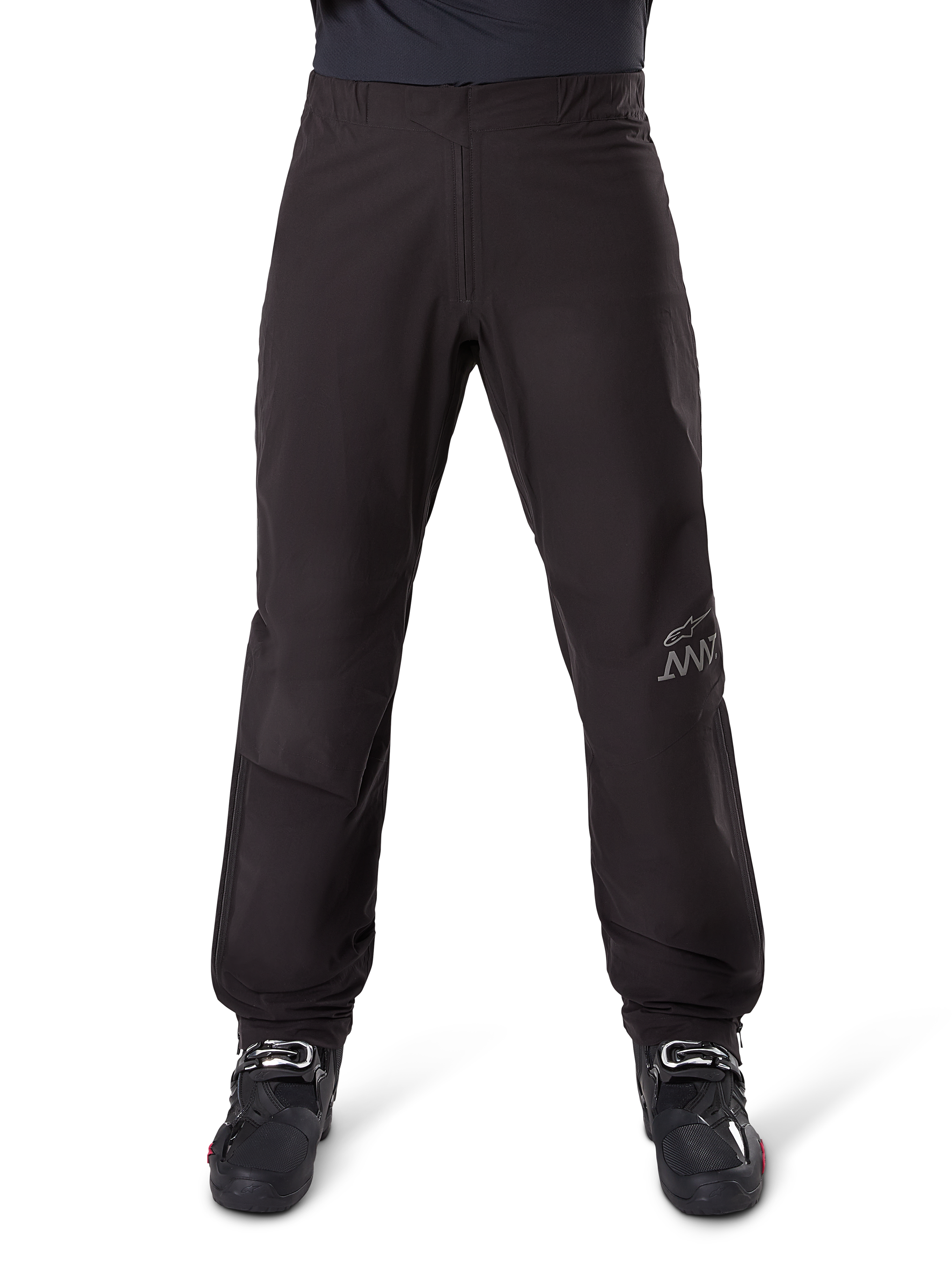 Alpinestars AMT-8 Stretch Drystar® XF byxfoder, svart, sedd framifrån buren med svarta motorcykelstövlar, med grå stjärnlogotyp och AMT-märkning på benet, mångsidiga vattentäta och vindtäta motorcykelkläder