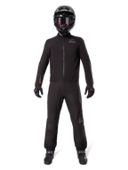 Motorcykelförare iförd Alpinestars AMT-8 Stretch Drystar® XF byxfoder och matchande jacka, helsvart vattentät och vindtät teknisk utrustning, svart hjälm, handskar och stövlar, stilren adventure touring-design.