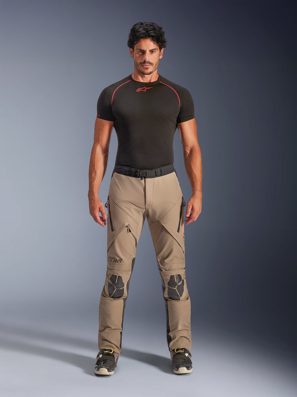 Manlig modell i Alpinestars AMT-8 Stretch Drystar® XF byxor i Walnut och Black, kombinerat med ett svart kortärmat baslager, äventyrsbyxor för touring med förstärkta knän, dragkedjeförsedd ventilation och ergonomisk stretchdesign.